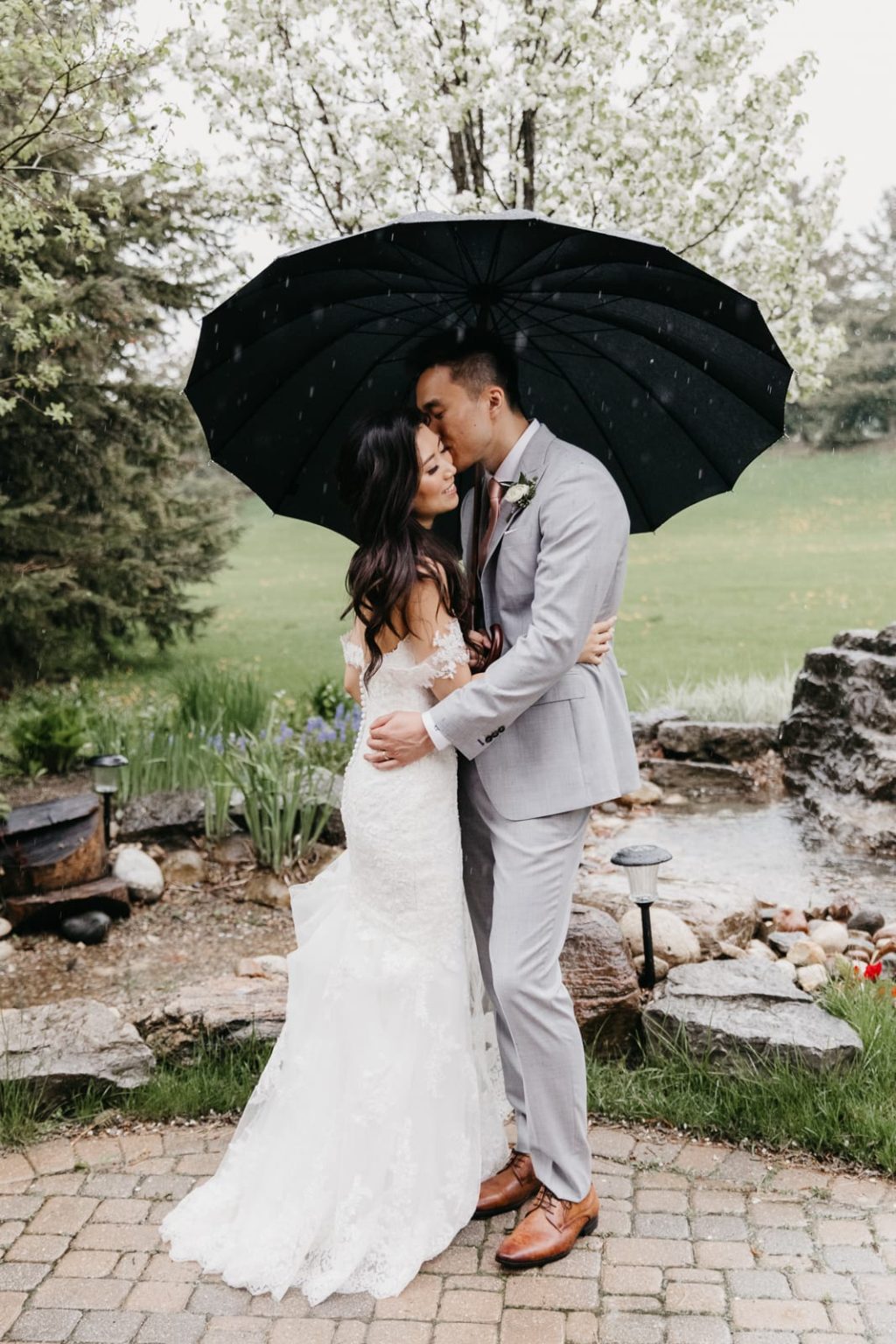 bride and groom kiss under umbrella in the rain