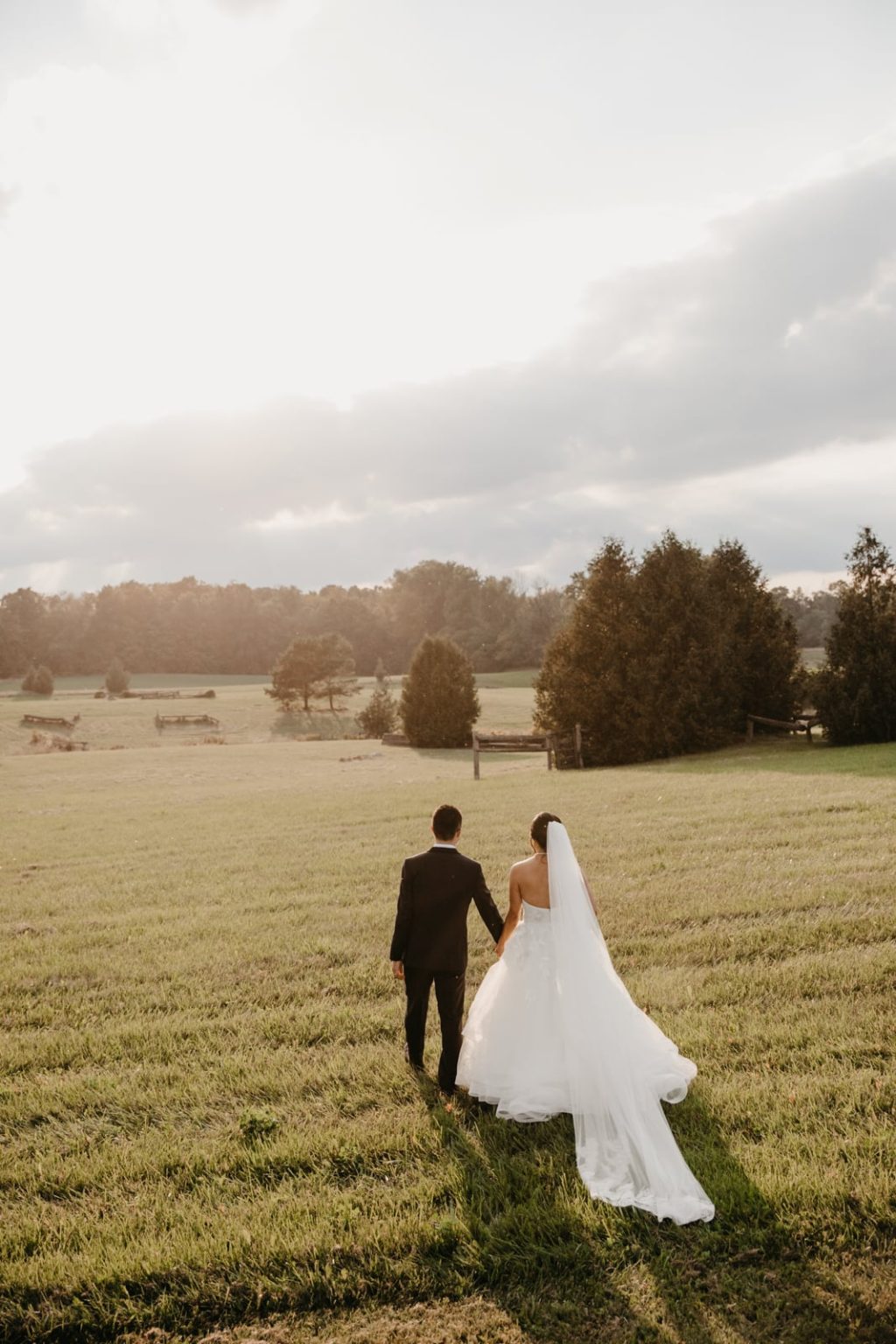 bride and groom walks into open field during sunset