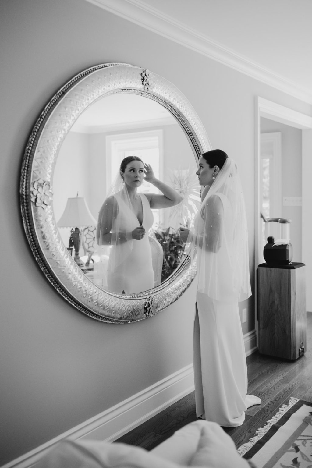 bride fixes hair in round mirror as she gets ready for wedding