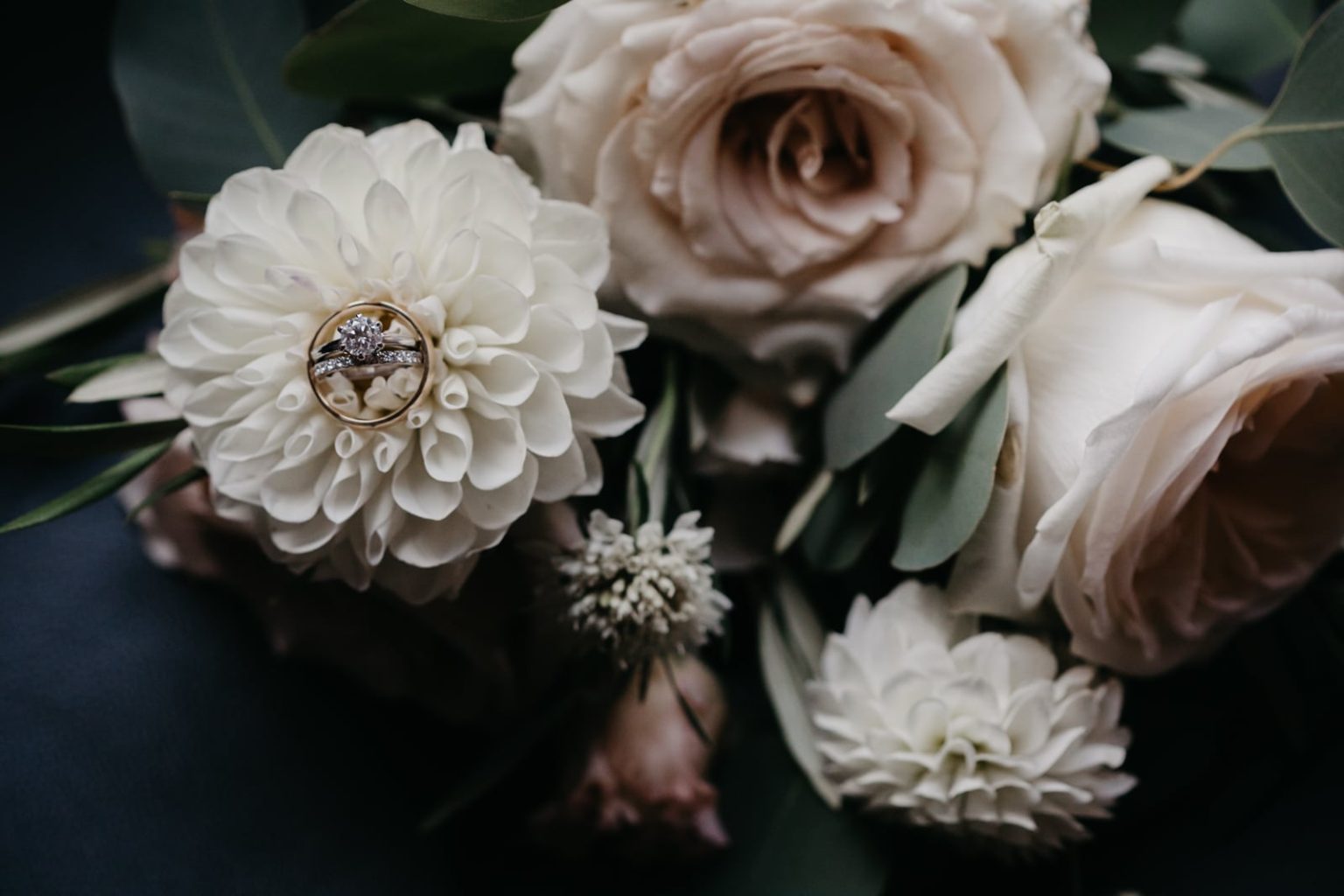 wedding rings in brides blush dahlia and rose bouquet